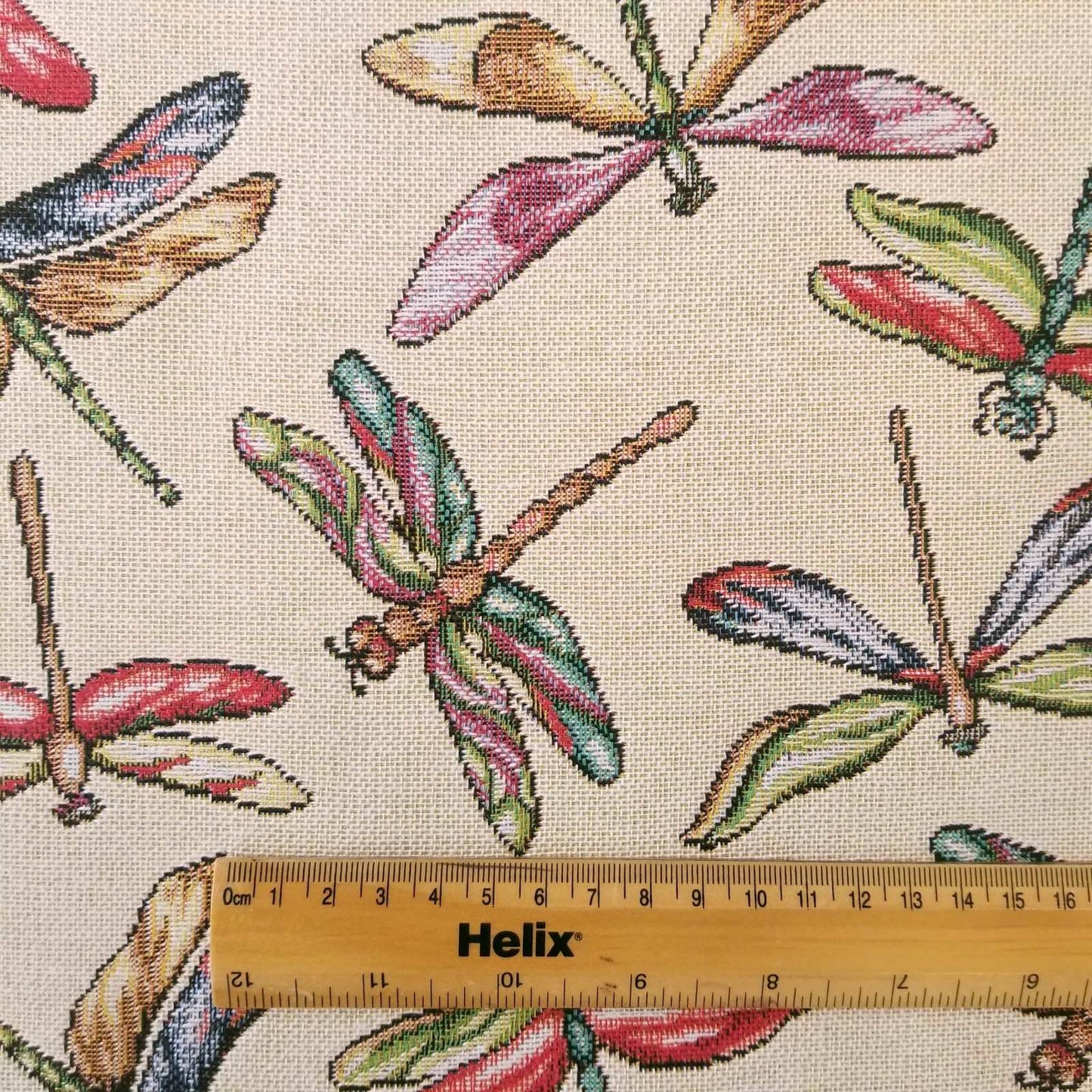 Cream tapestry fabric with a rule showing scale of colourful dragonfly design