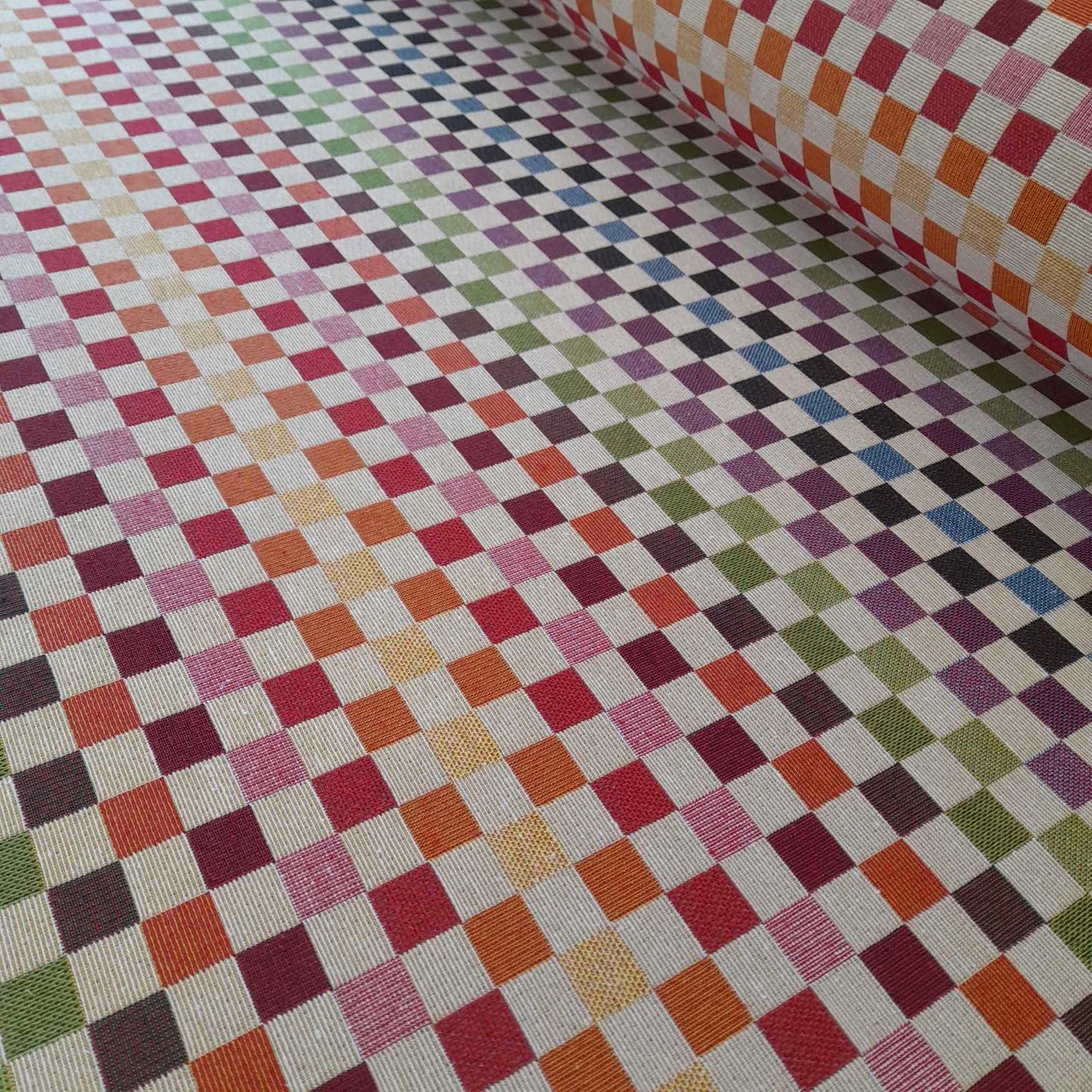 A roll of tapestry fabric with small squares in rainbow colours