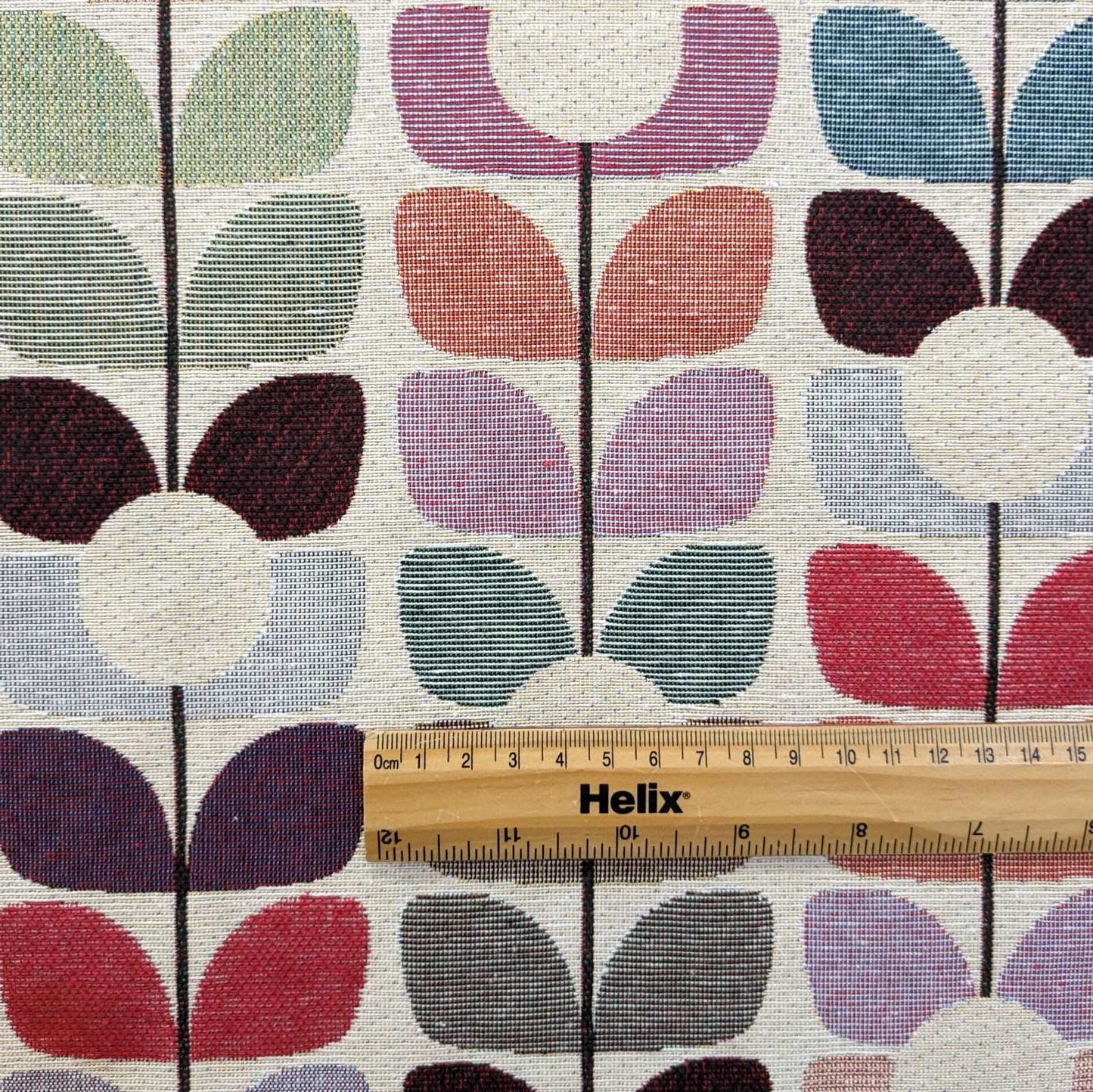 Tapestry fabric with a rule showing scale of colourful leaf sprig design