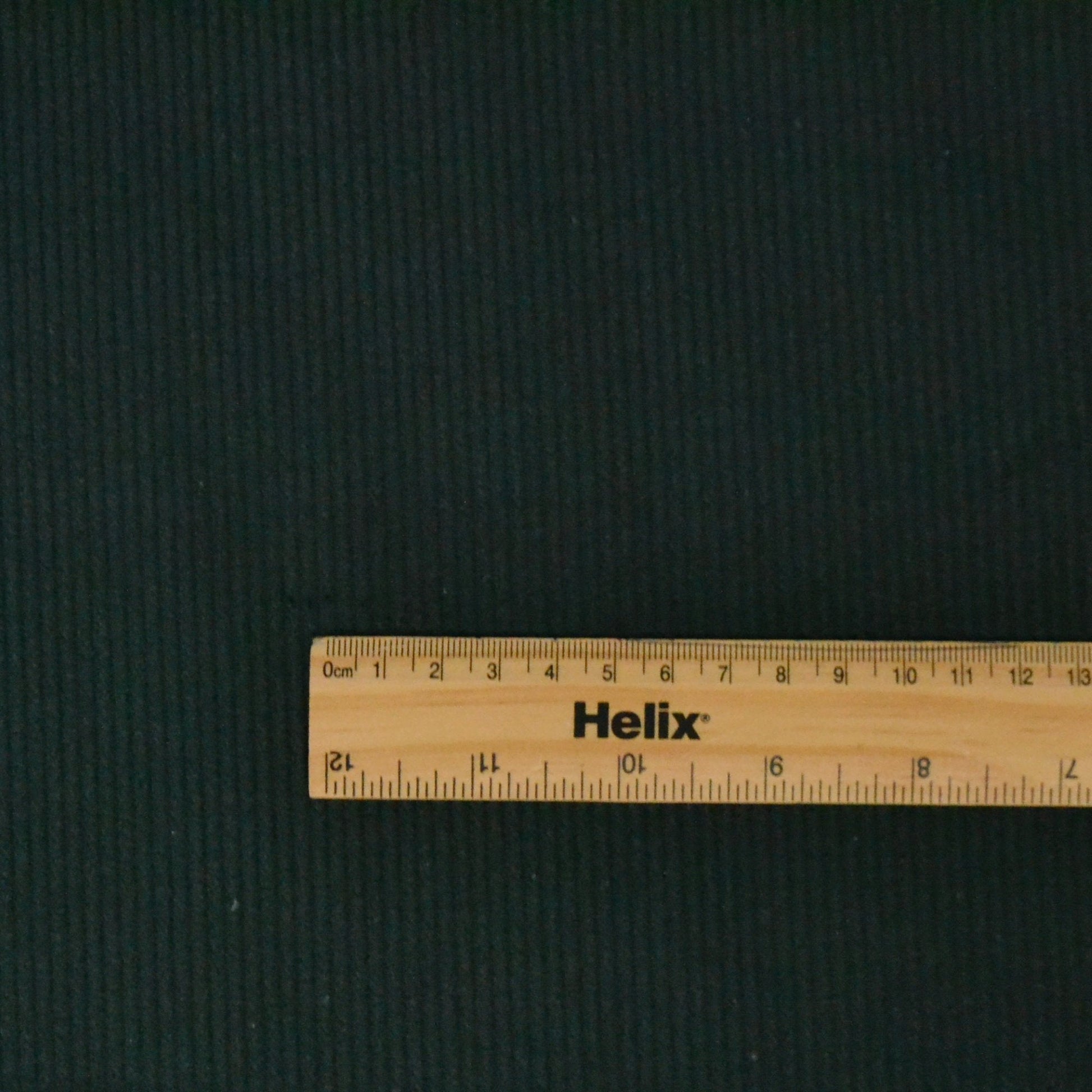 Bottle Green corduroy fabric with a ruler showing the size of the ridges in the fabric
