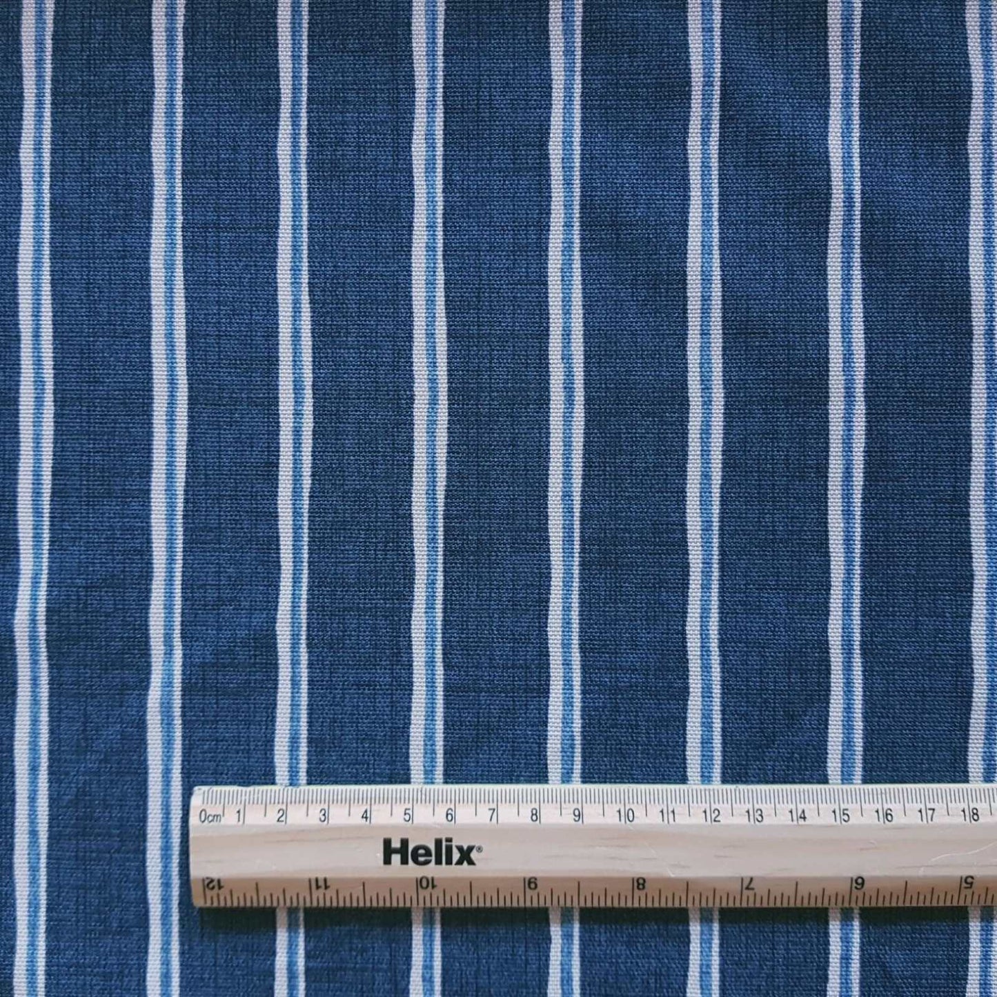 Midnight blue colour curtain fabric with a rule showing size of of white and lighter blue stripes